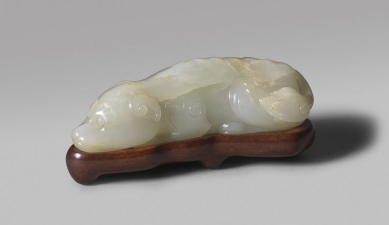 A pale celadon jade carving of a recumbent dog with fitted wood stand (Song/early Yuan dynasty)