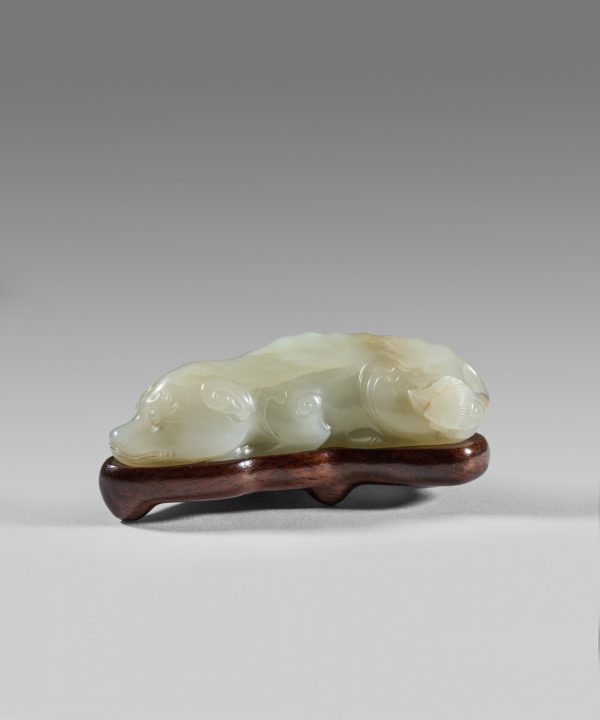 A pale celadon jade carving of a recumbent dog with fitted wood stand