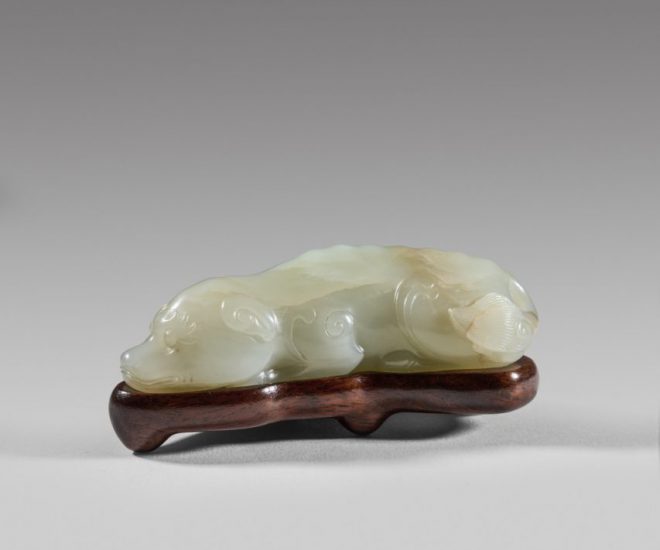 A pale celadon jade carving of a recumbent dog with fitted wood stand
